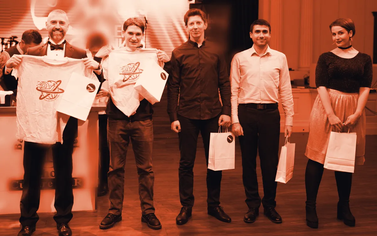 Five Intersog colleagues on stage holding gift bags; two hold up white T-shirts printed with the snail-and-globe logo